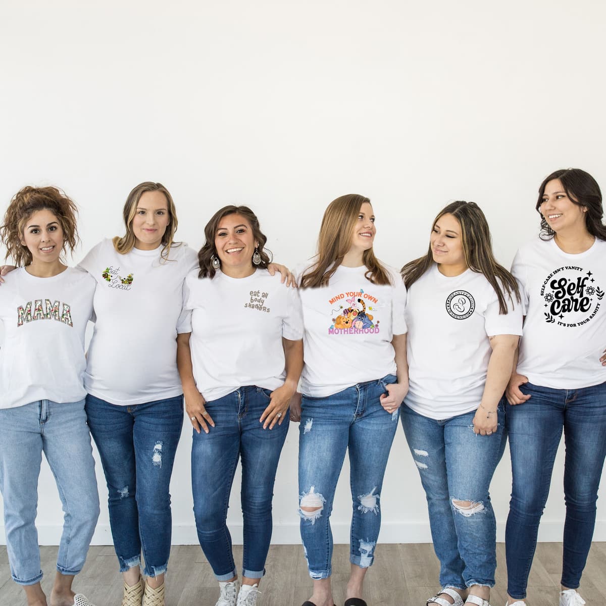 Six women side by side in white Milk Magique tees, each wearing a different design